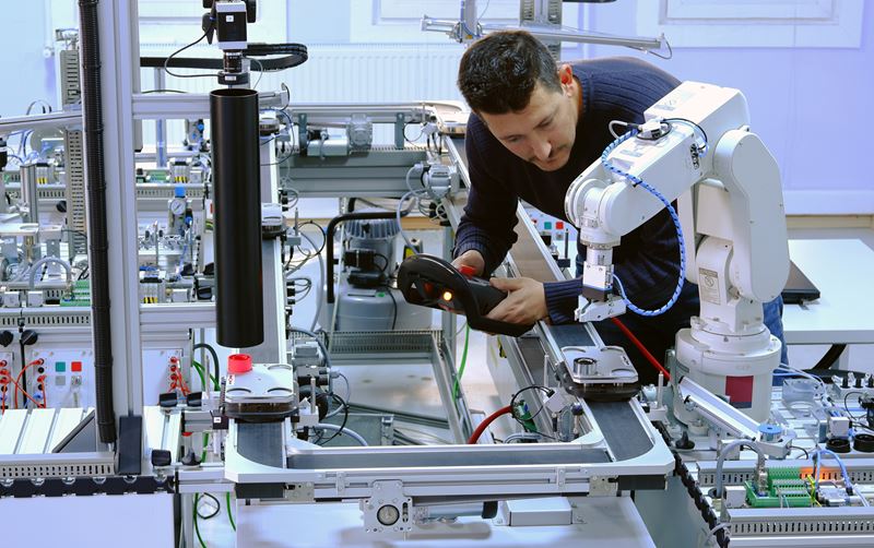 Un homme programme un bras robotique dans une usine
